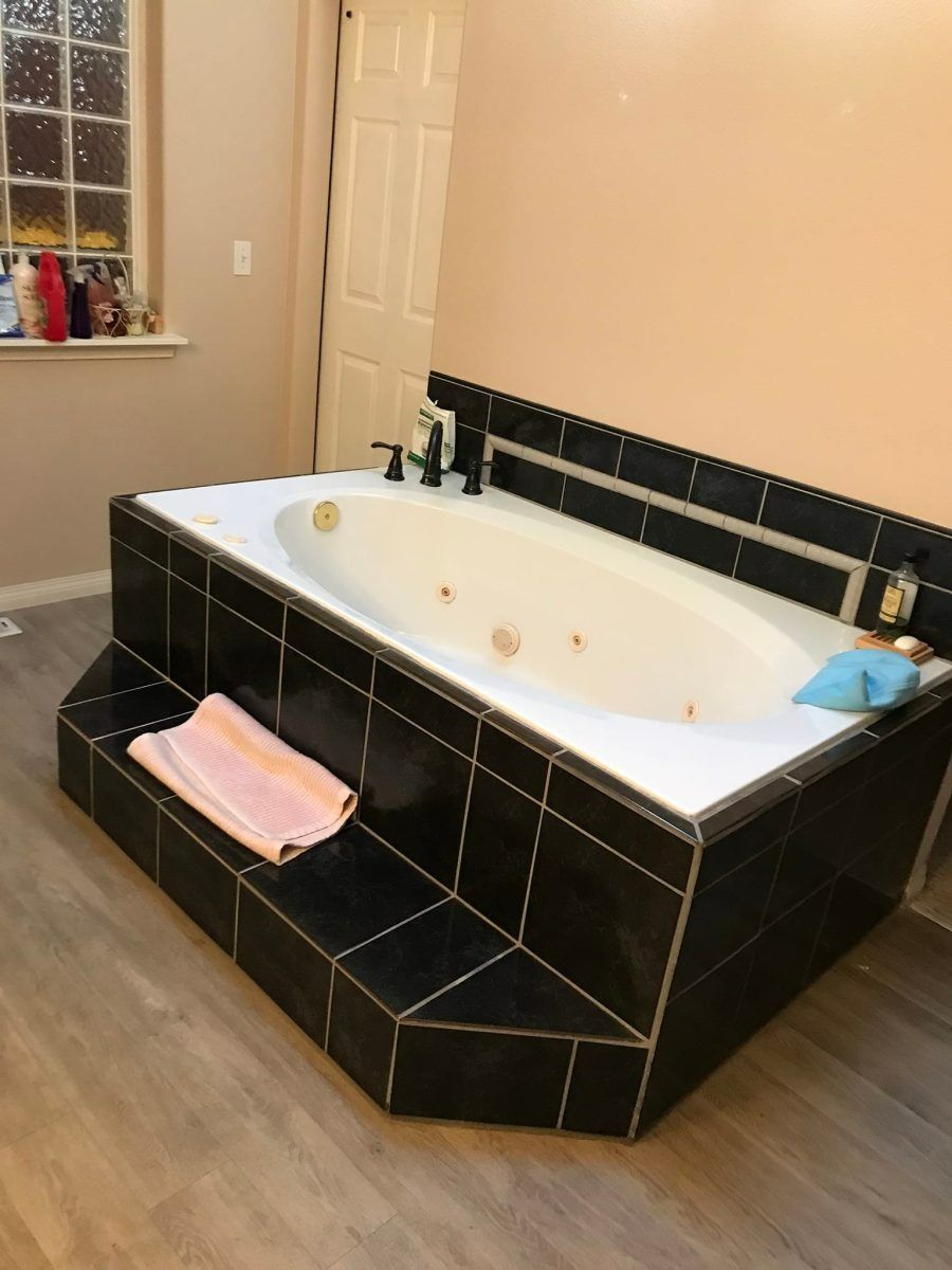 Black tiled bathroom with a built-in white soaking tub and a pink towel on the front ledge.