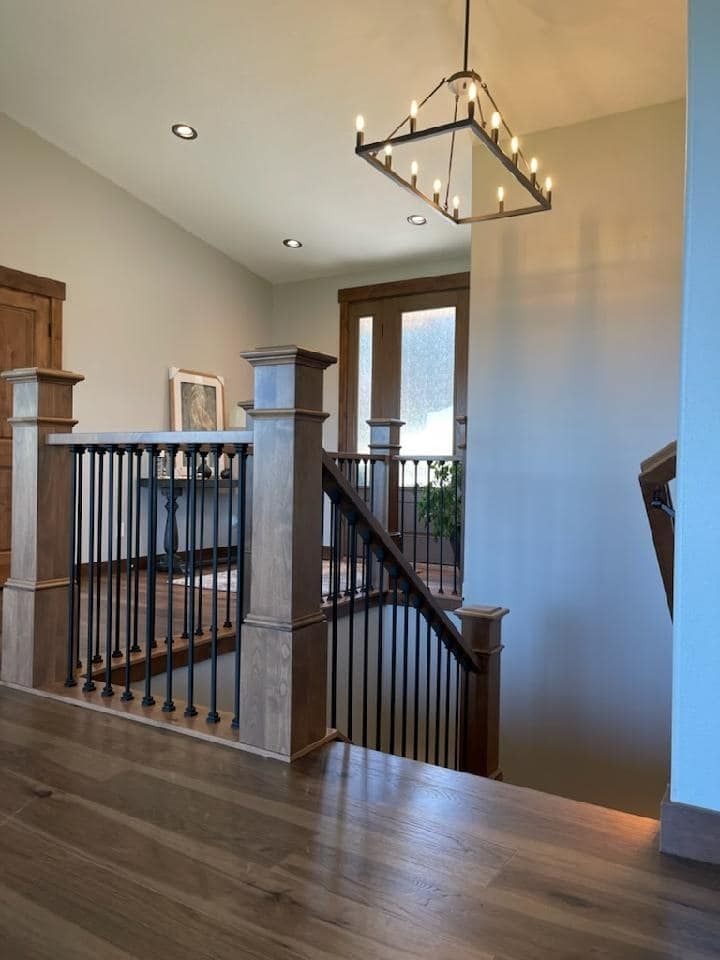 Staircase landing with wood floors, black railing, and modern chandelier in a bright home interior