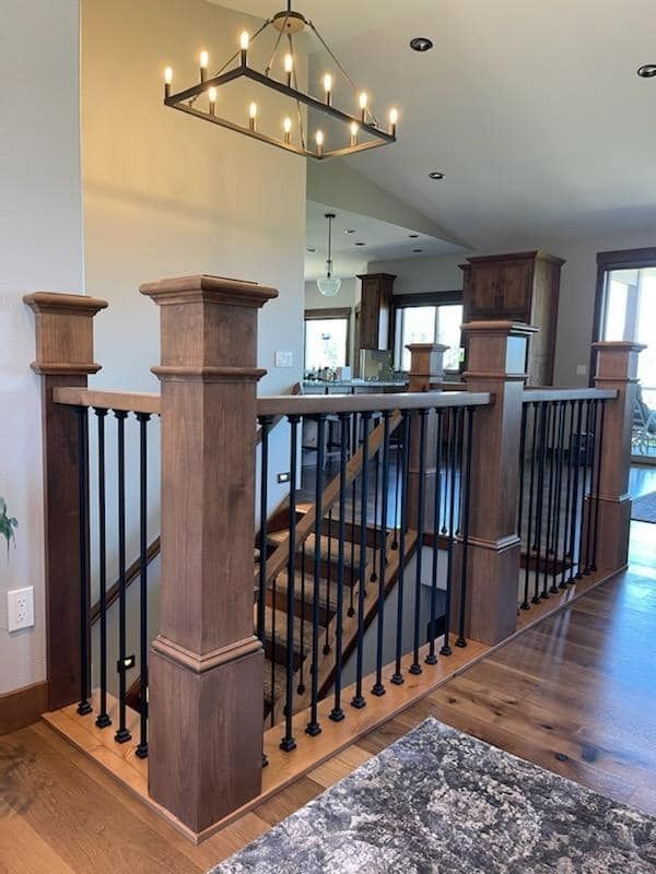 Staircase landing with black railings, wooden posts, and a modern chandelier in a home interior