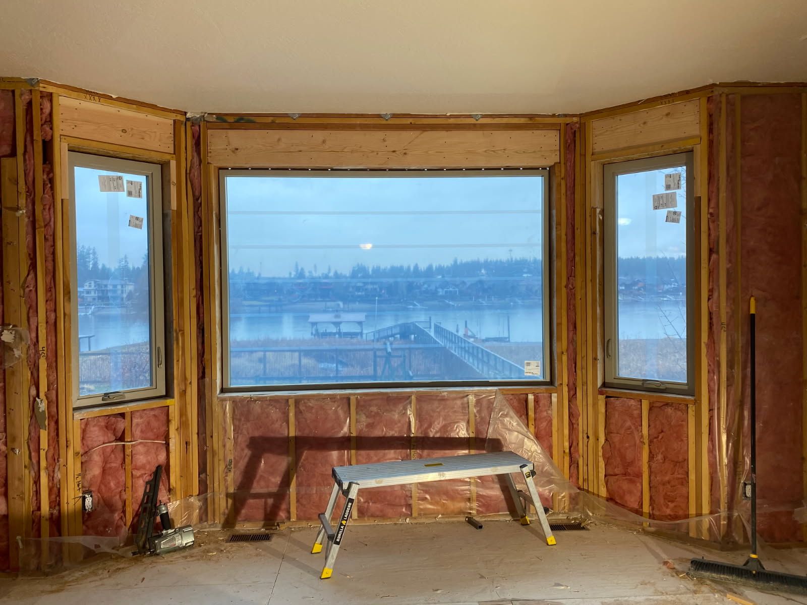 Unfinished room with exposed studs, a large bay window, and a workbench in the center.
