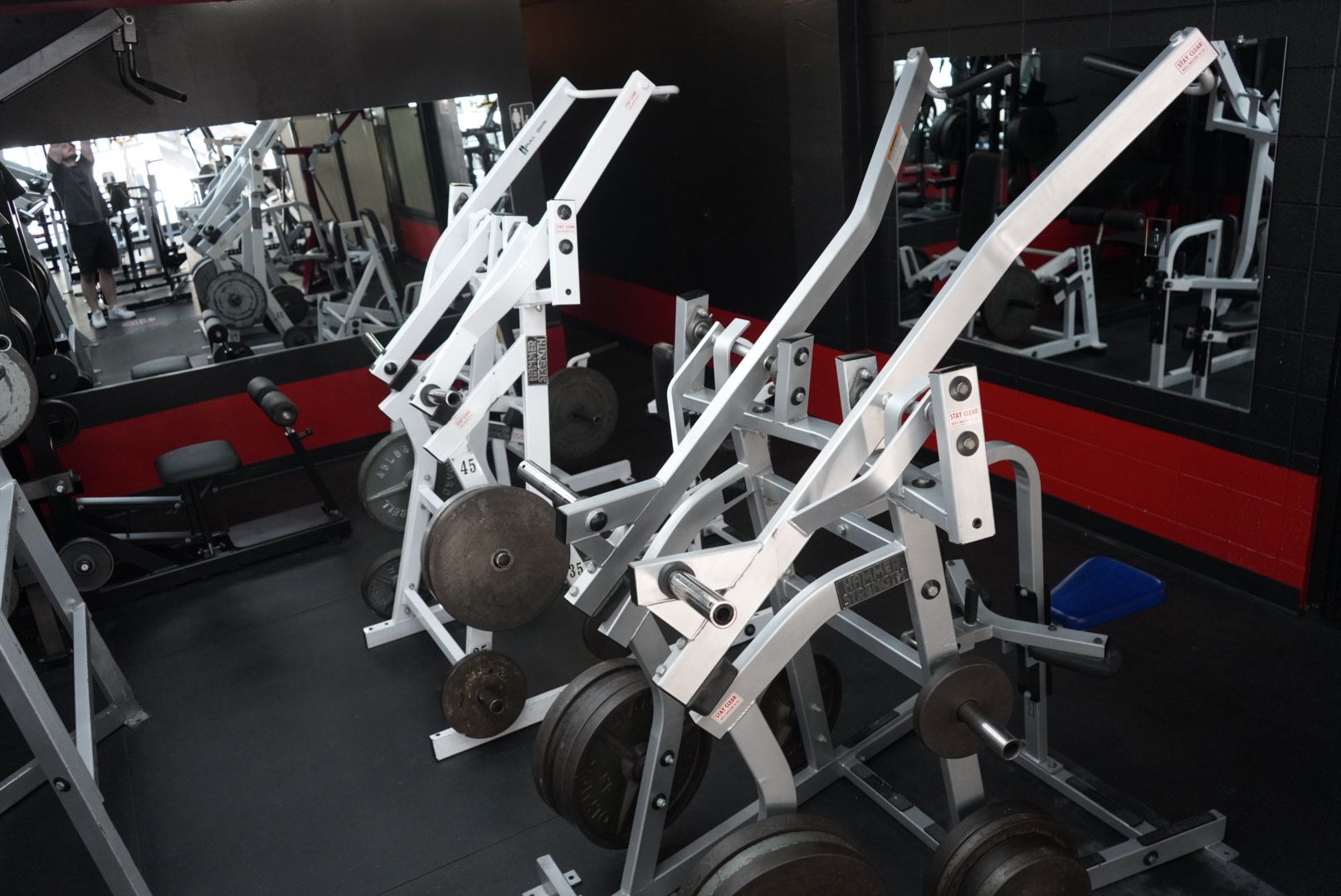 Gym interior with white exercise machines, mirrors, and black-and-red flooring