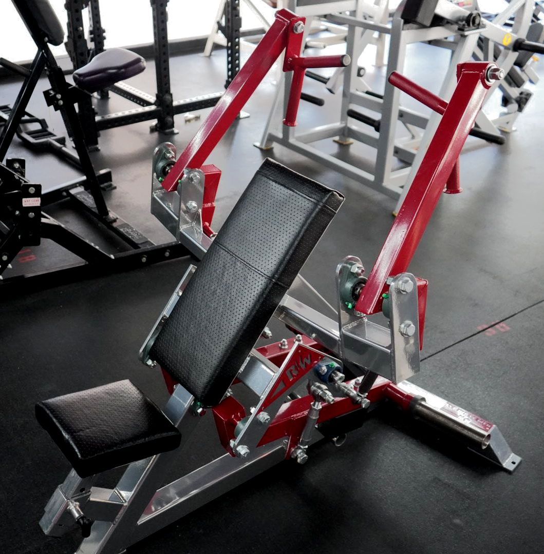 Red and black adjustable weight bench in a gym, angled with padded seat and backrest.