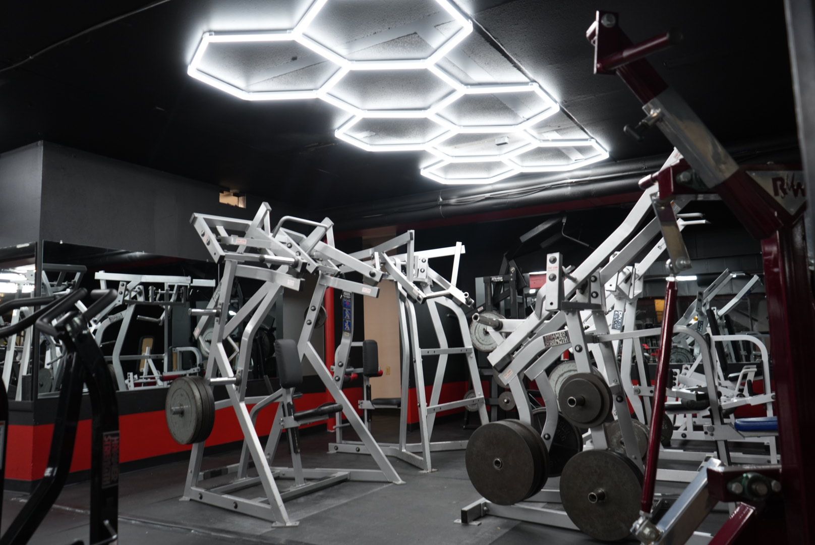 Modern gym interior with strength machines, free weights, and bright hexagonal ceiling lights