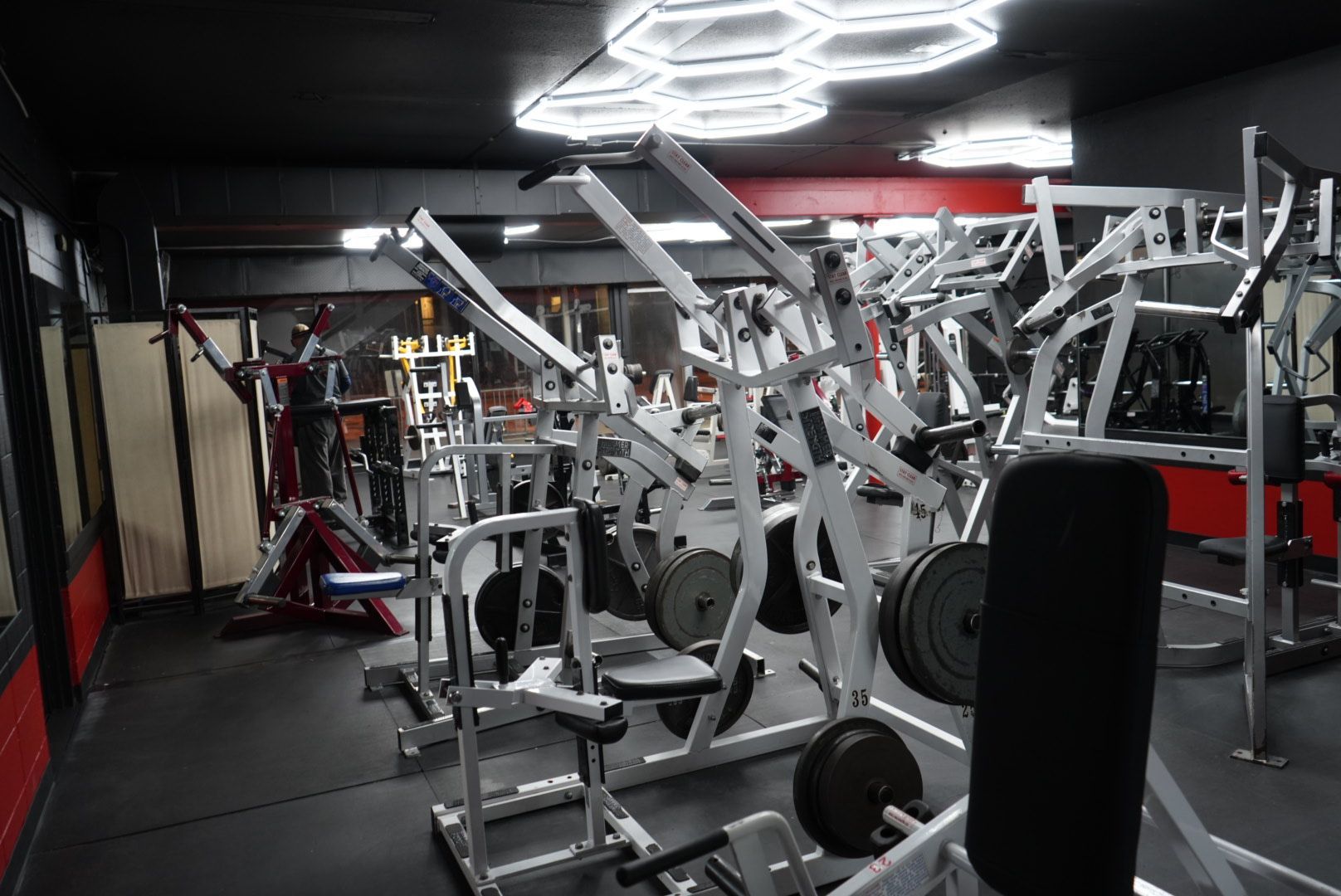 Dimly lit gym with rows of weight machines and red-and-black walls