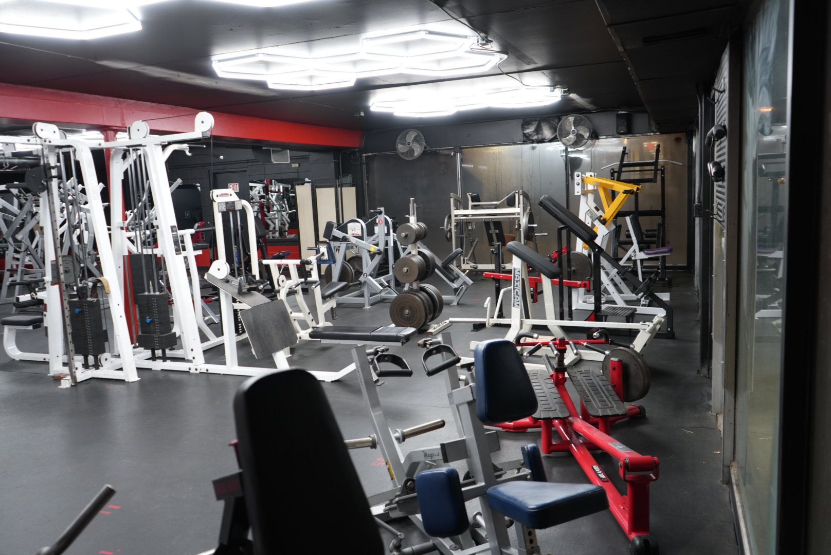 Empty gym interior with exercise machines, benches, and red-and-white equipment under bright lights