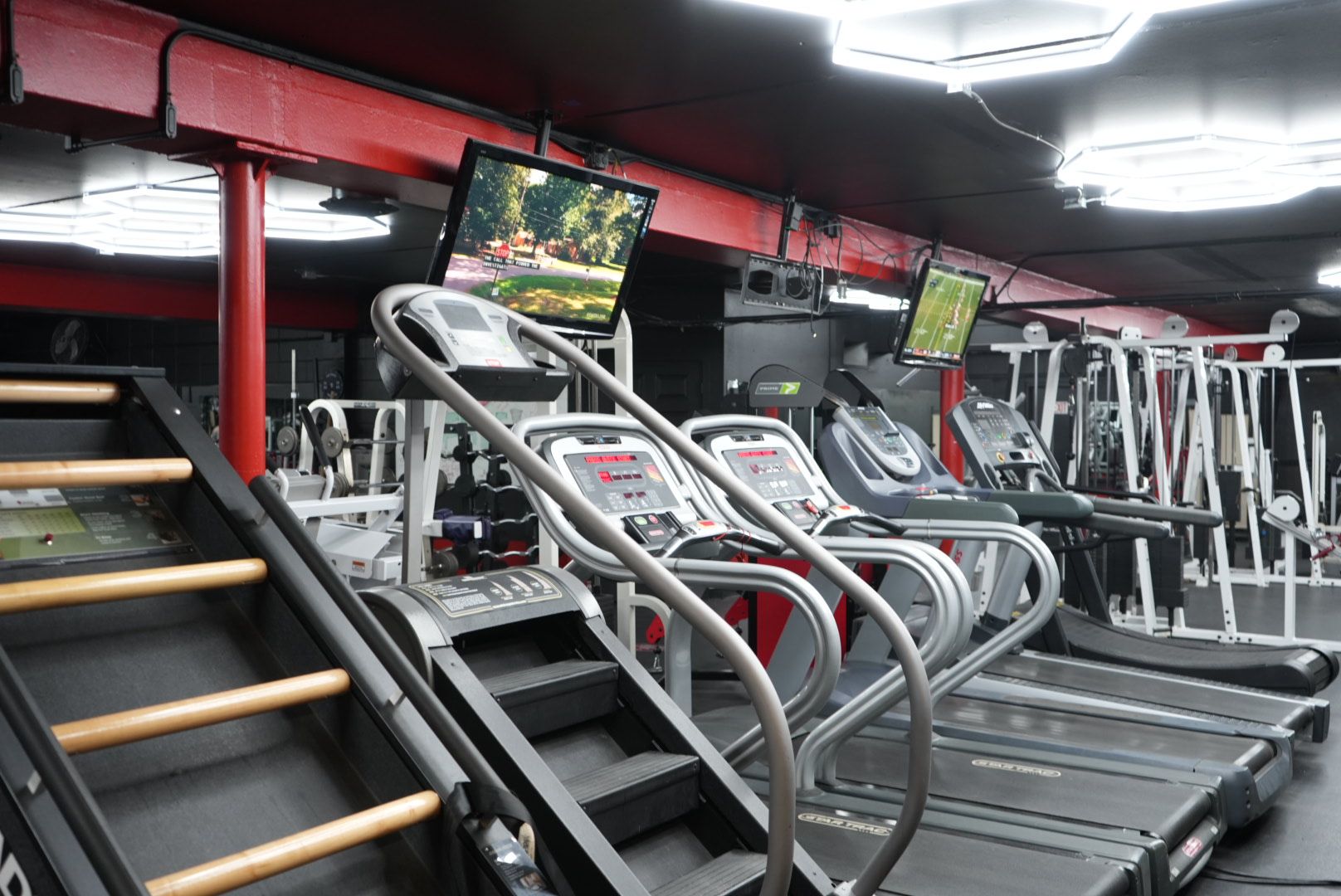 Rows of treadmills in a gym, with red walls and wall-mounted TVs above them