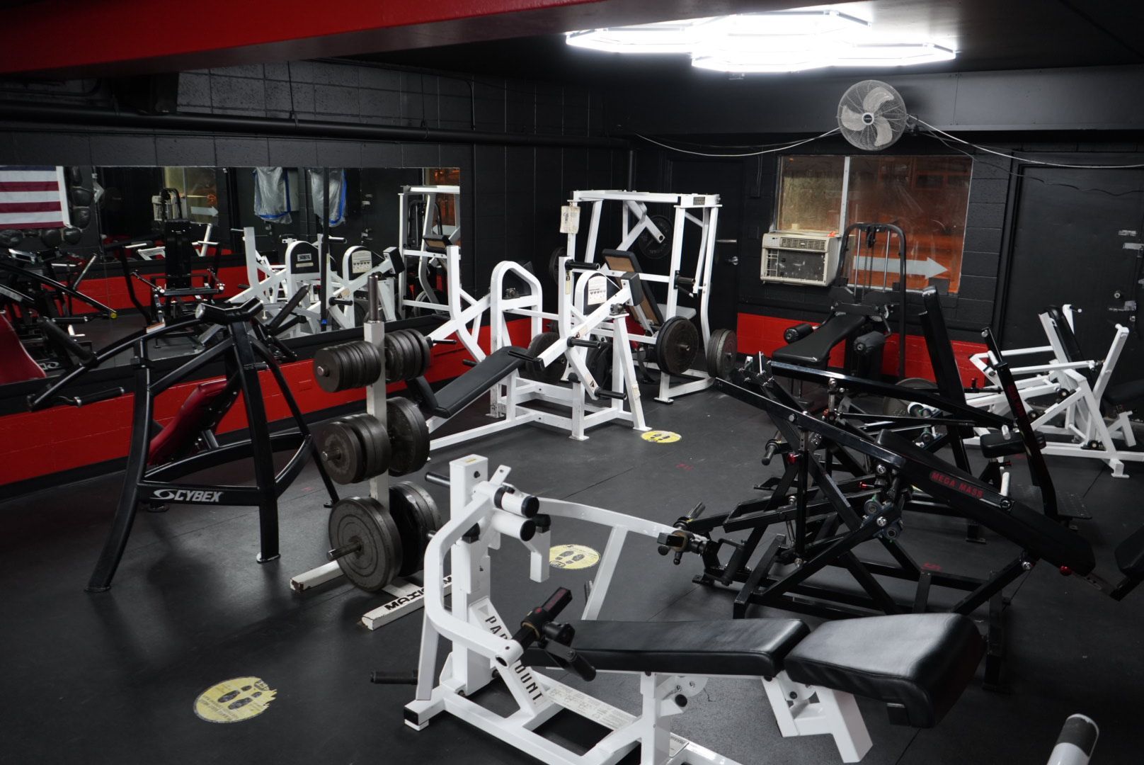 Gym interior with black and red equipment, mirrors, and weight machines under low lighting