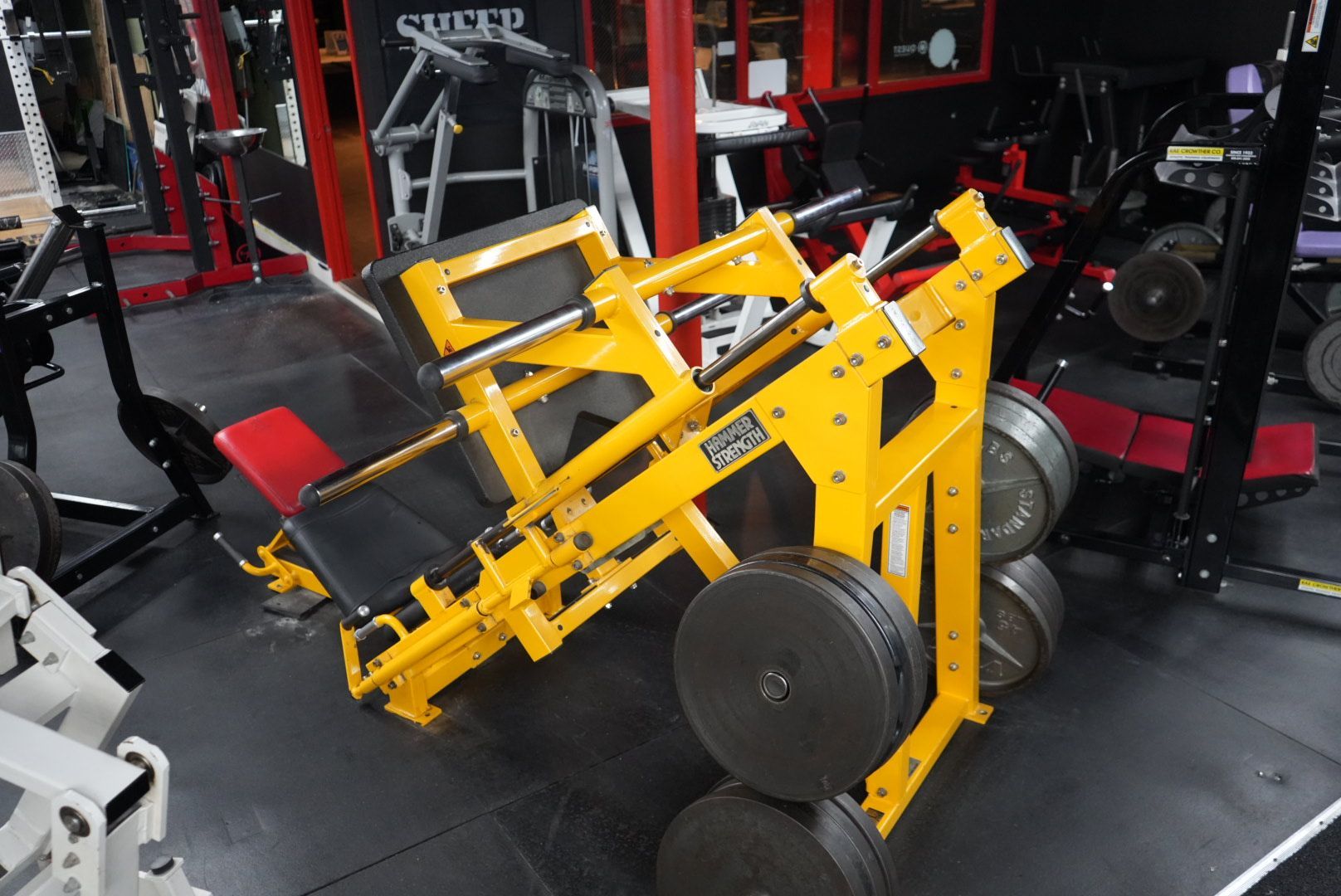 Yellow leg press machine in a gym with black and red equipment around it