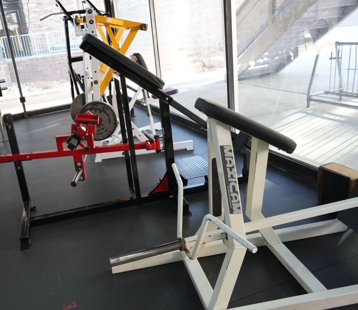 Gym equipment with a white exercise machine, red bench, and black mat on a workout floor.