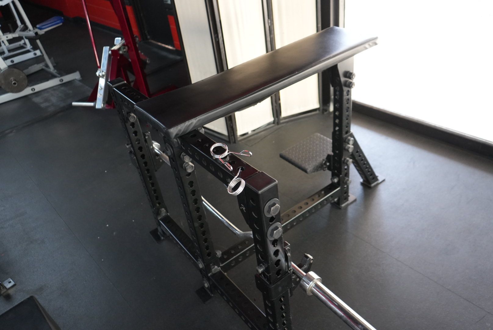 Weight bench with black padding and metal frame in a gym, with a barbell resting on the rack