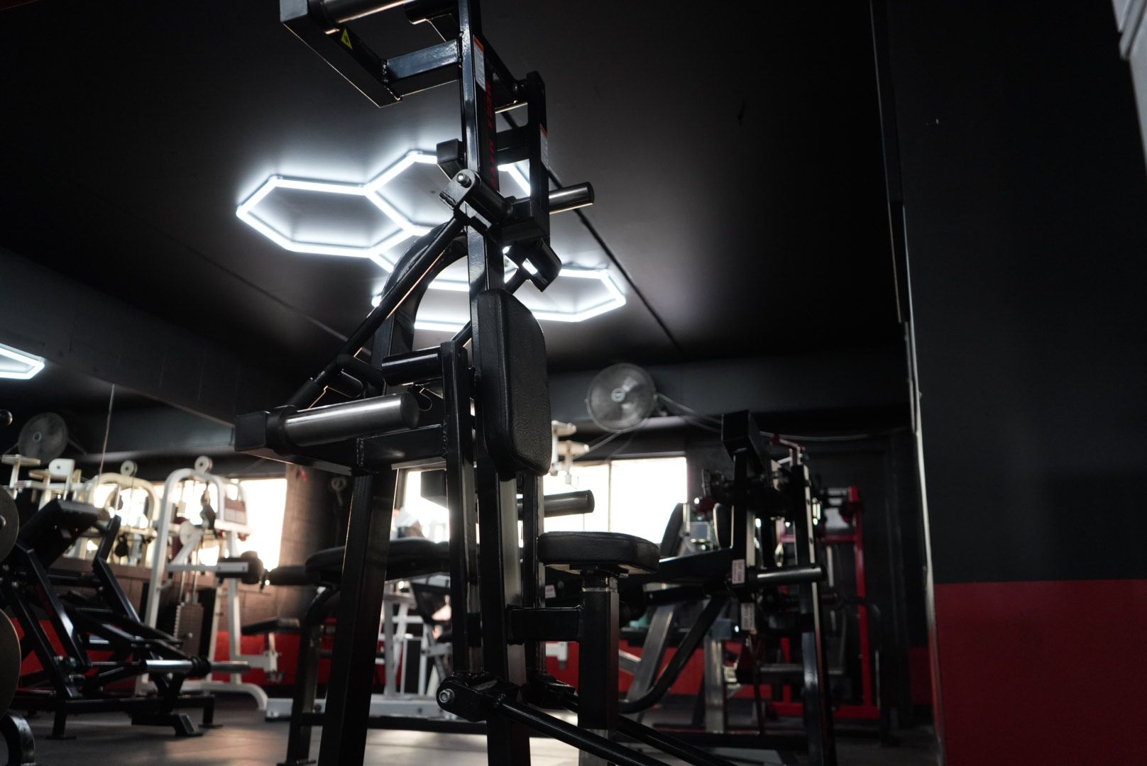 Dim gym interior with strength machines and bright hexagonal ceiling lights