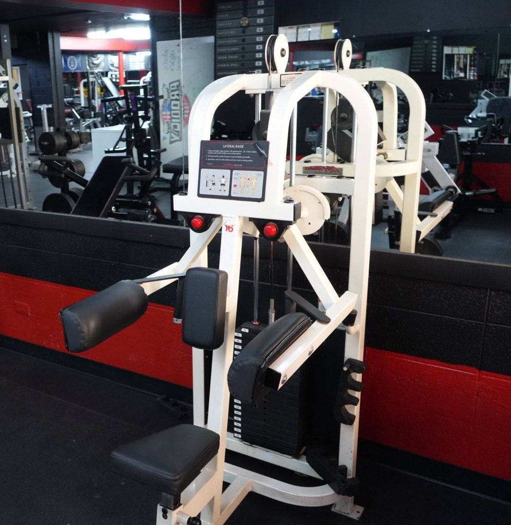 Weight machine in a gym, with black and white padded seats and a red wall in the background.