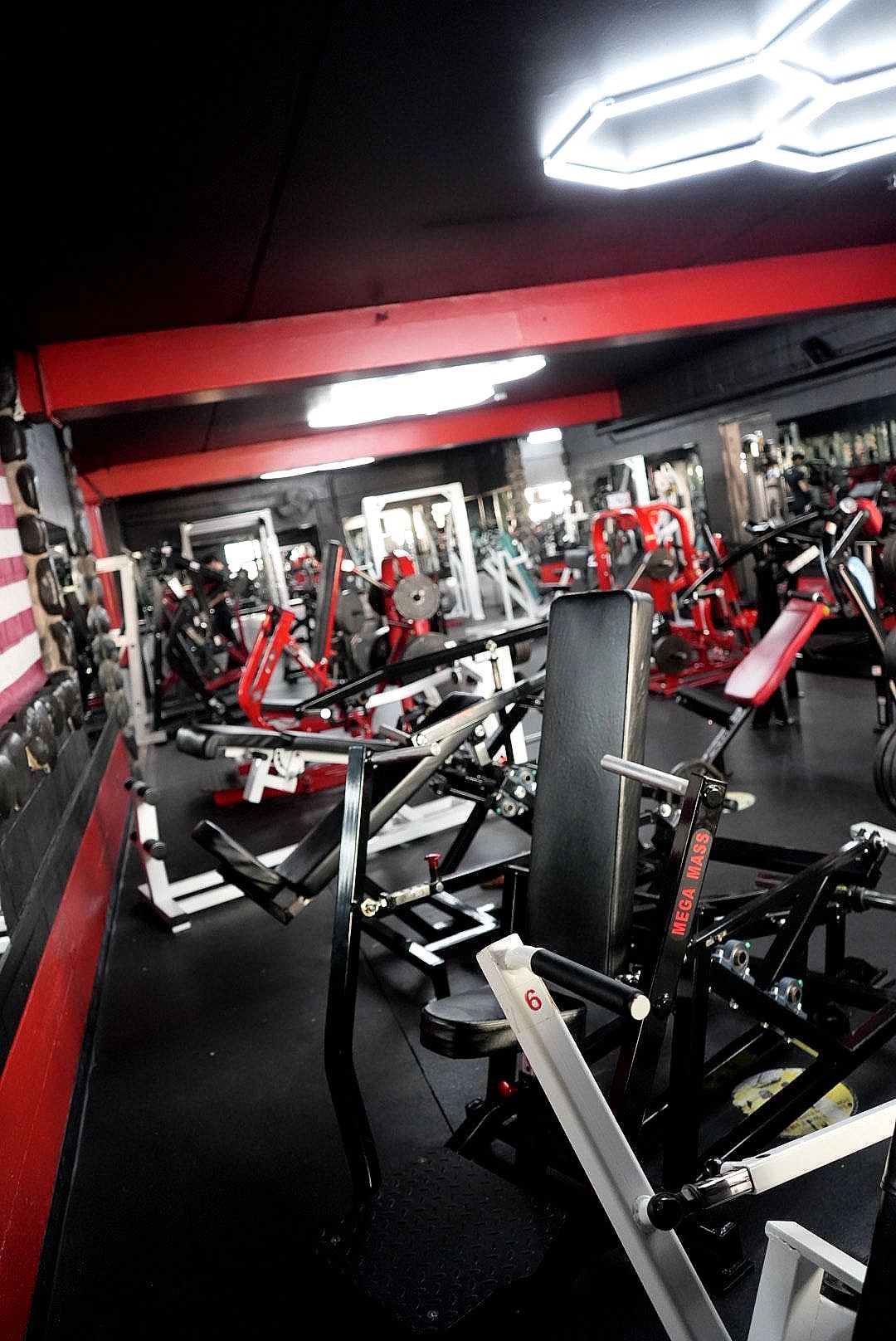 Dim gym interior with rows of red and black weight machines and mirrors under bright ceiling lights