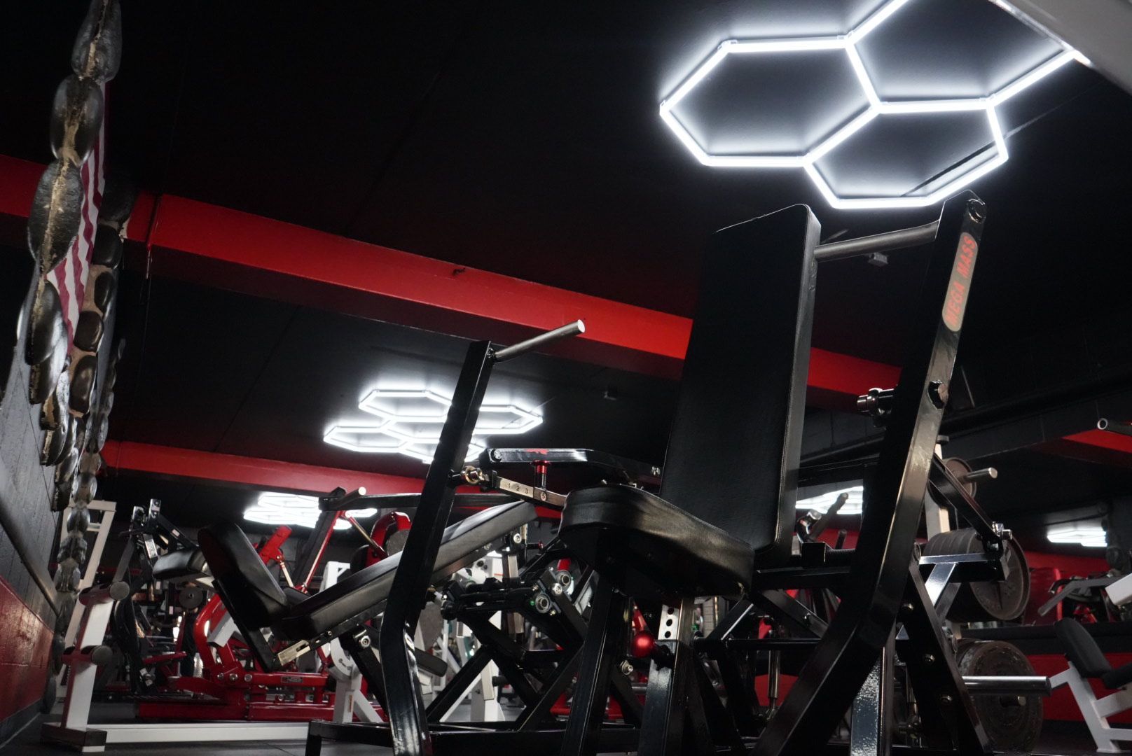 Modern gym interior with red lighting, mirrors, weight machines, and hexagonal LED ceiling lights