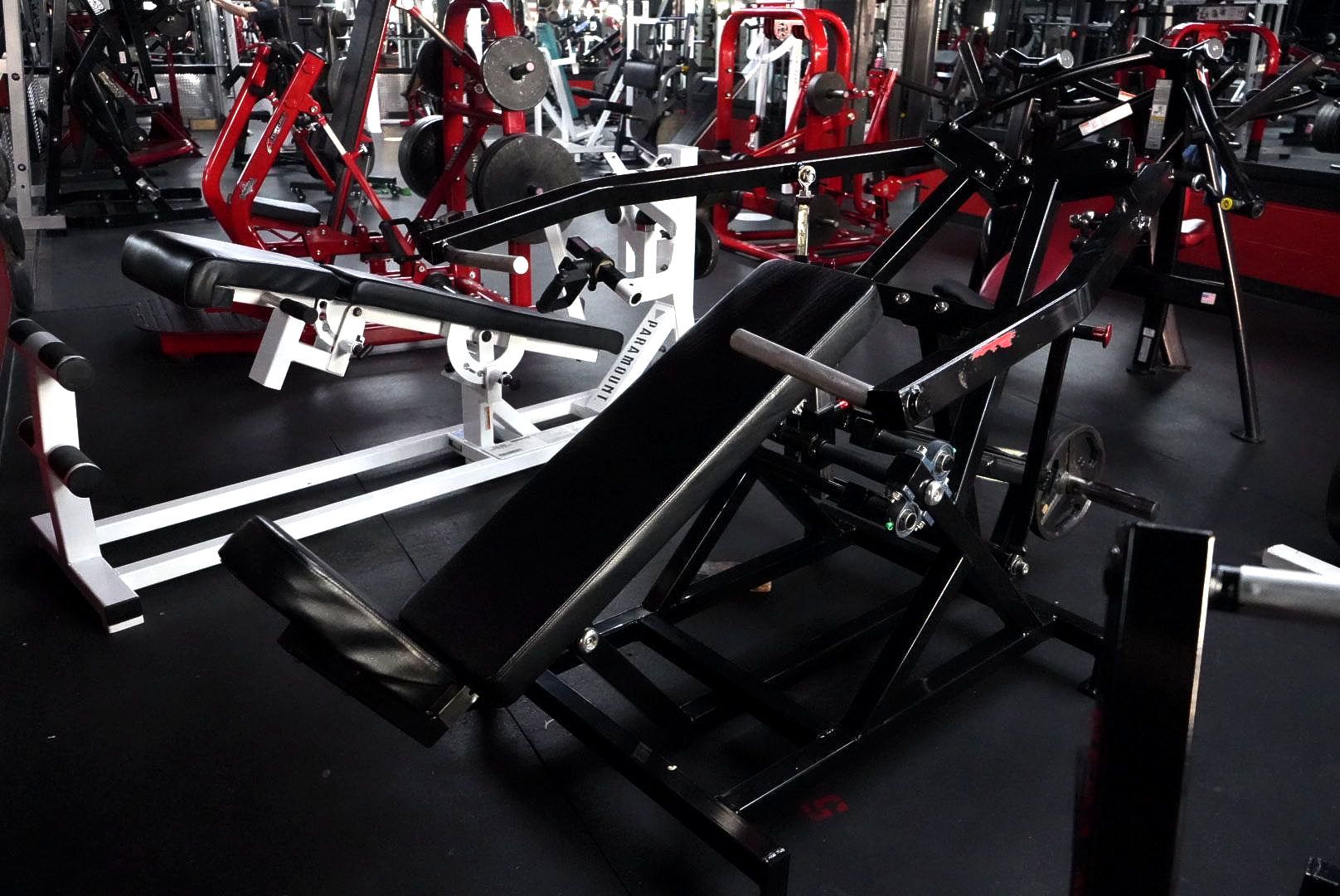 Black incline leg press machines in a gym with red and white equipment.