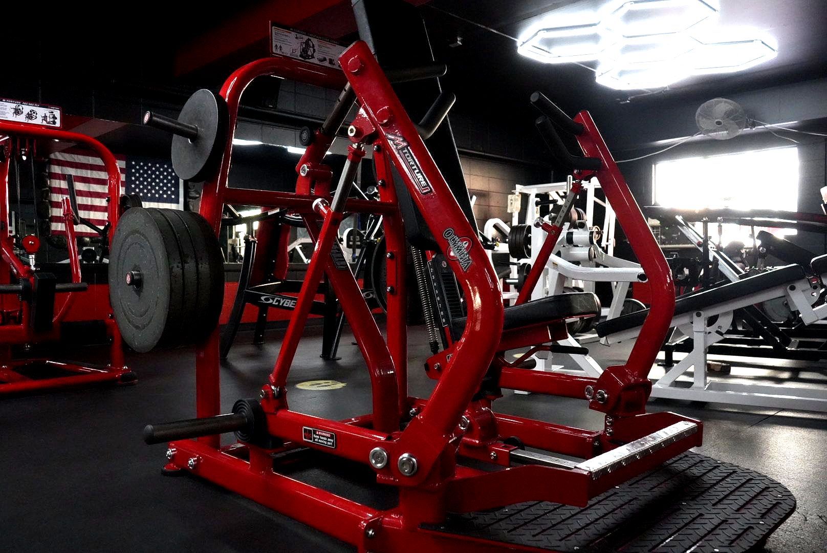 Red weight machine in a gym with black floor mats and bright overhead lights