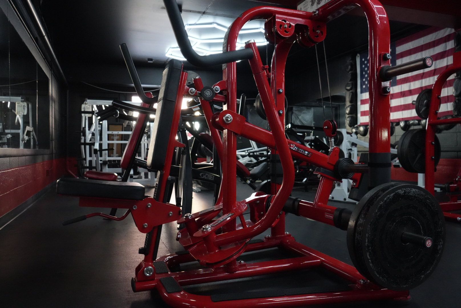 Red gym equipment frame with large tire in a dim gym, American flag mural on the wall