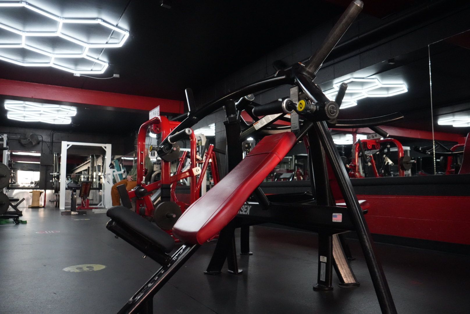 Modern gym interior with red and black workout machines under bright geometric ceiling lights