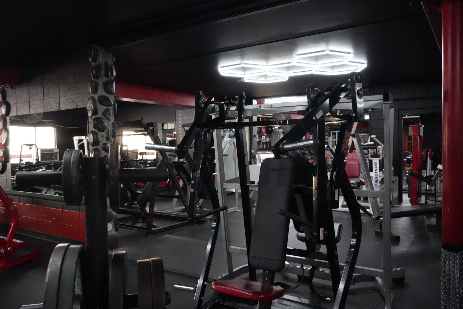 Dimly lit gym with black-and-red weight machines and equipment spread across the room