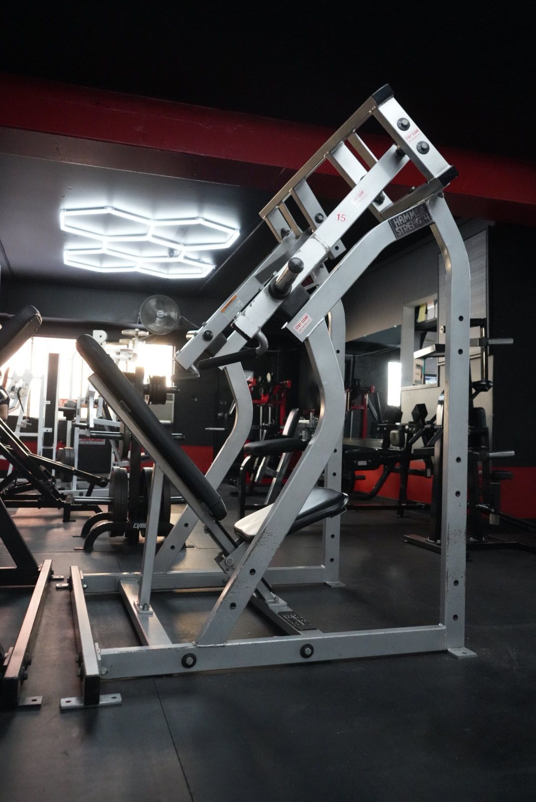 Incline leg press machine in a gym, silver frame with black padding and red walls.