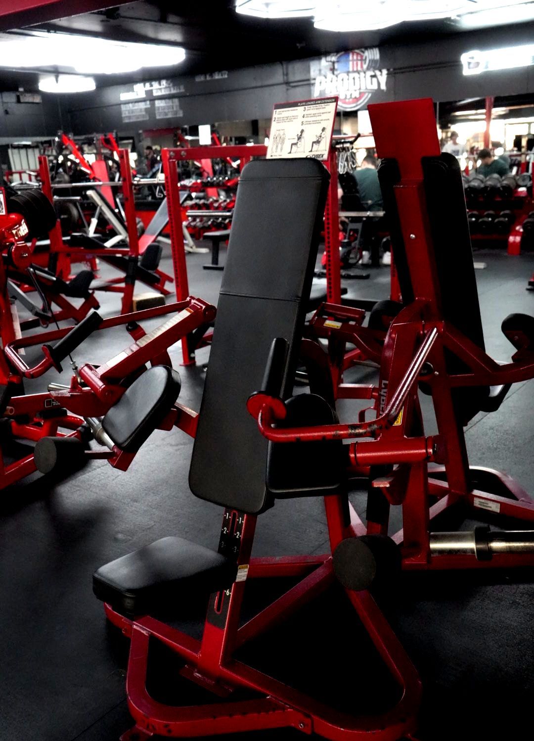 Red gym exercise machine with black padding in a dimly lit fitness room