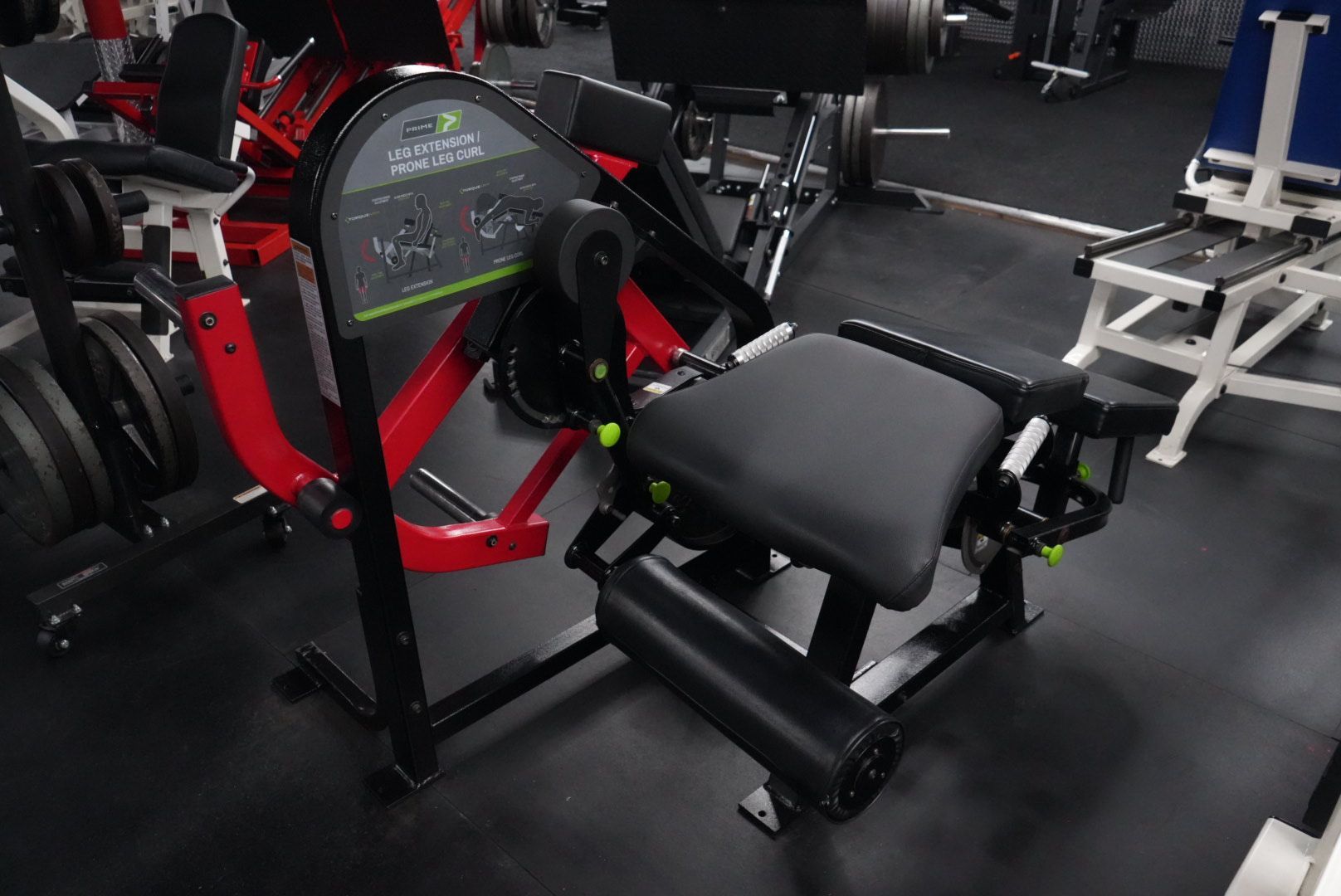 Gym equipment with a black padded machine seat and red frame on a rubber floor in a fitness center