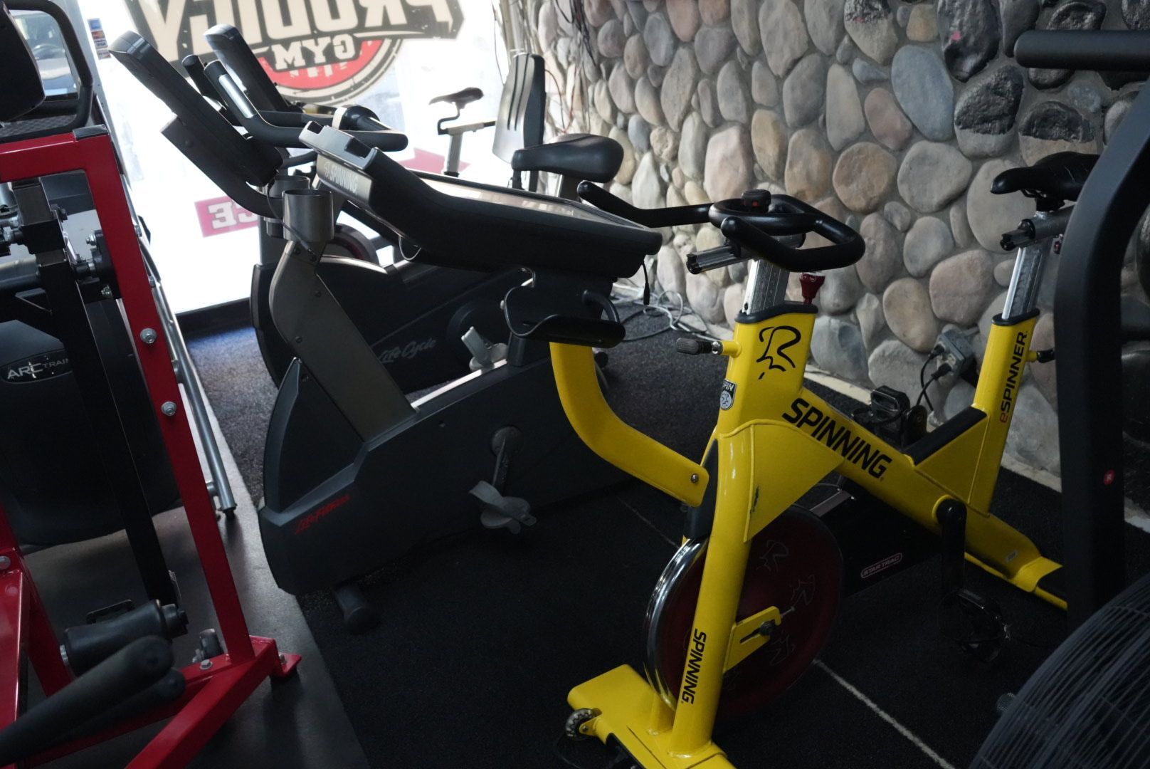 Yellow stationary bikes in a gym by a stone wall, with a treadmill and exercise equipment nearby