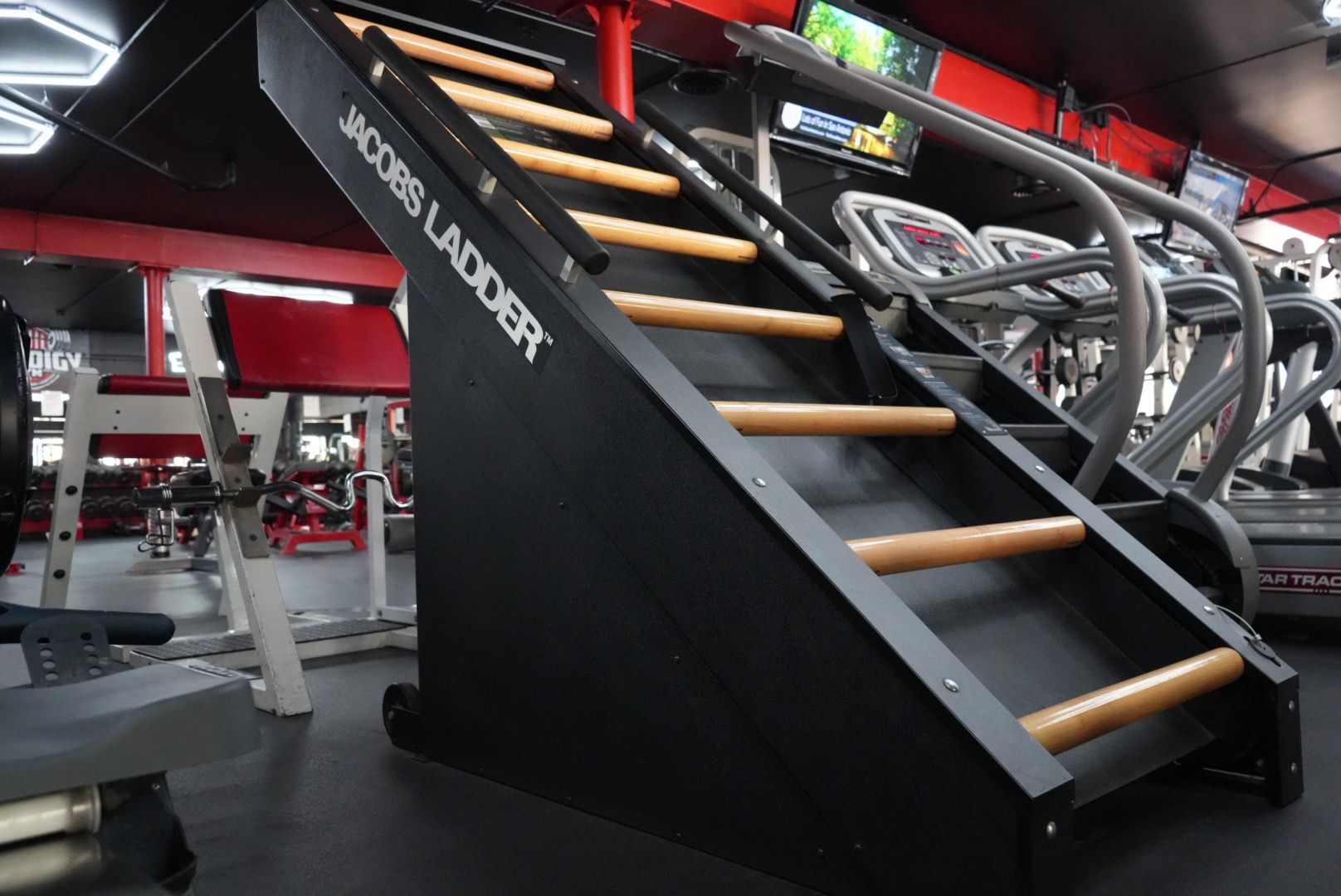 Indoor gym sled track with a metal stair-climb machine and wooden steps, viewed from below