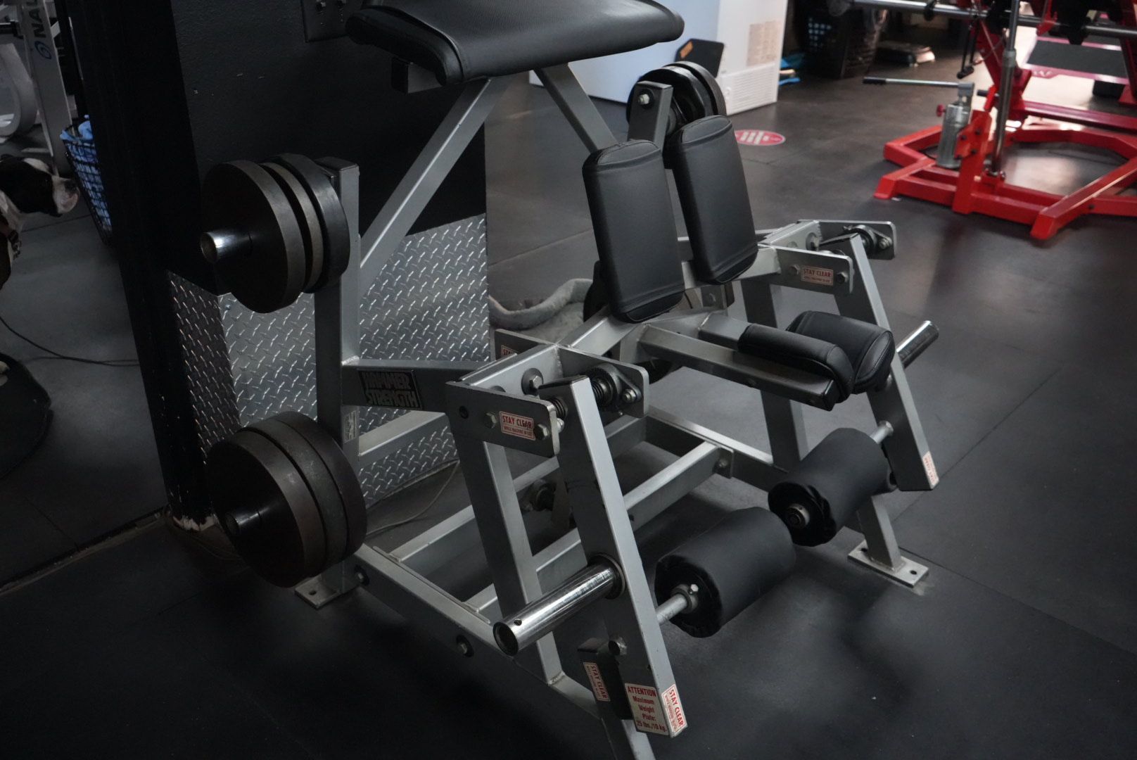 Gym weight machine with black and silver padded supports in a fitness room