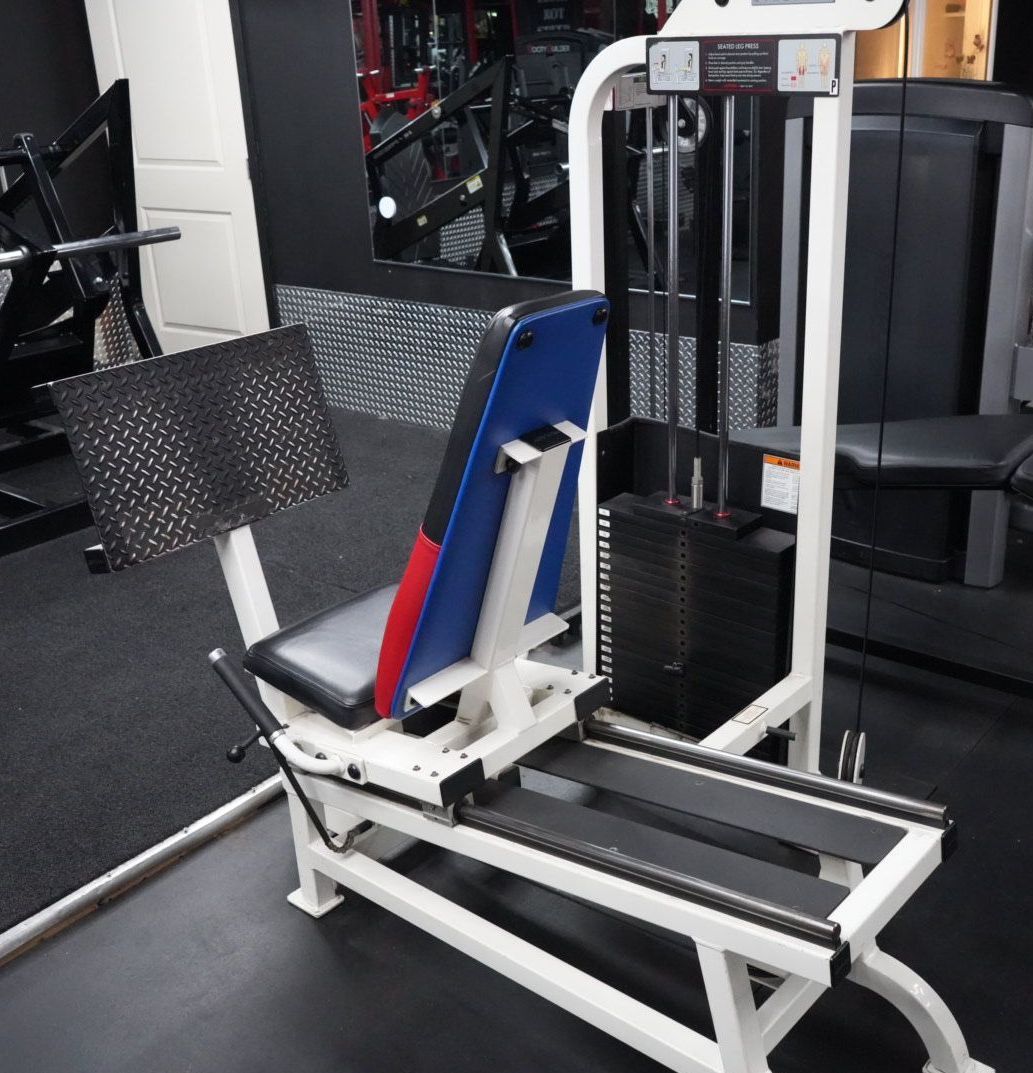 Gym leg press machine with white frame and black seat in a fitness center