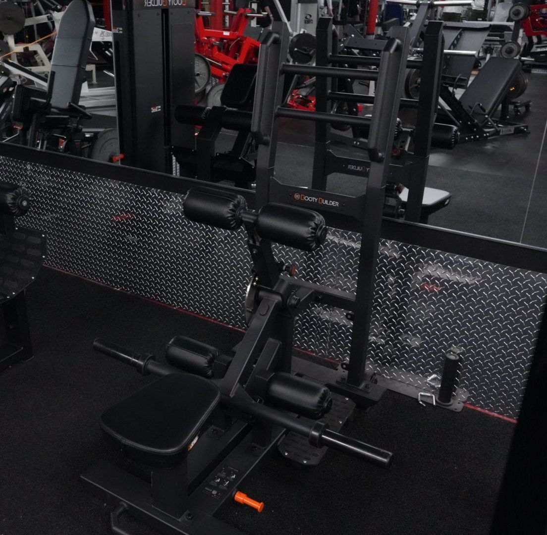 Gym weight machine with black padding and metal frame in front of a mirrored wall.