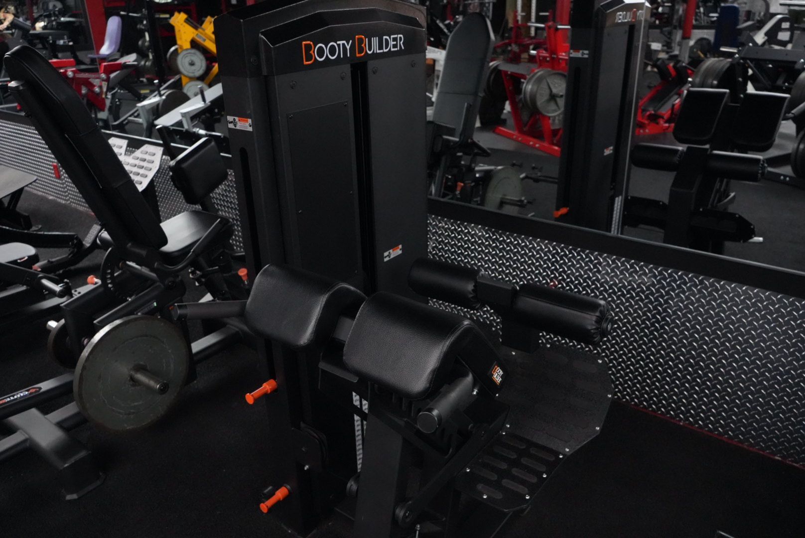 Gym machine with black padding and a mirrored wall in a fitness center