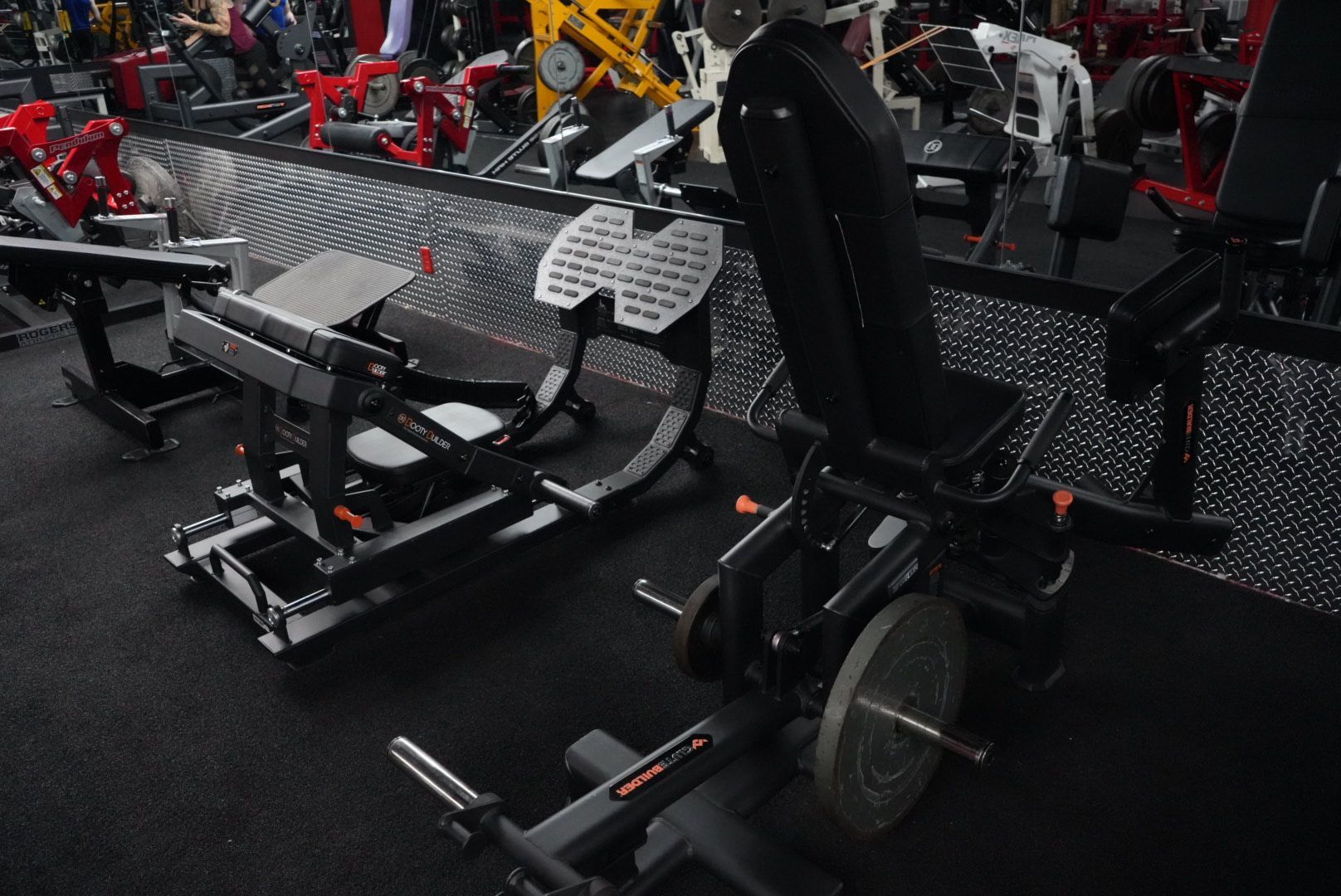 Rows of gym equipment, including black exercise machines and benches, in a weight room.