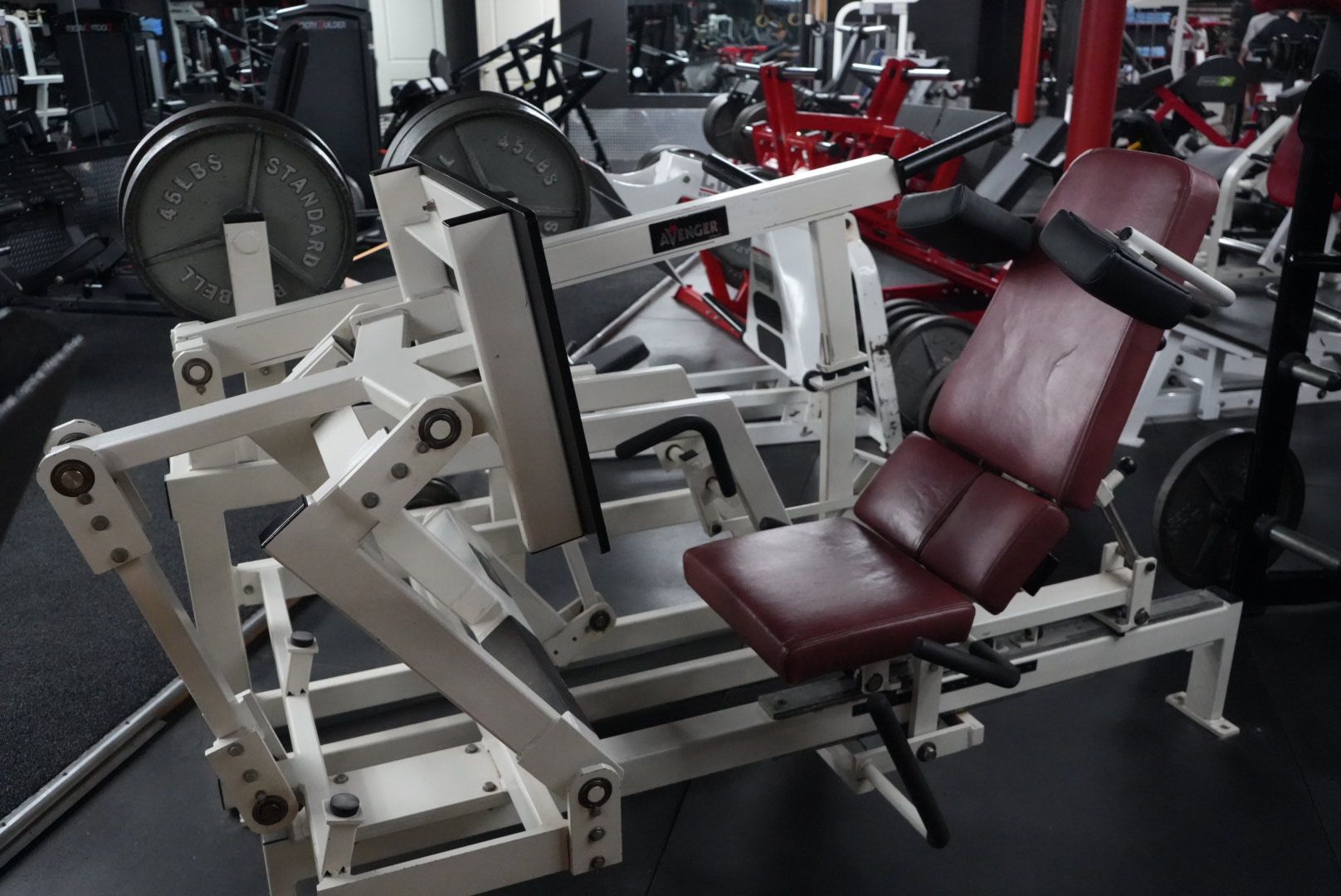White gym leg press machine with maroon padded seat in a fitness room