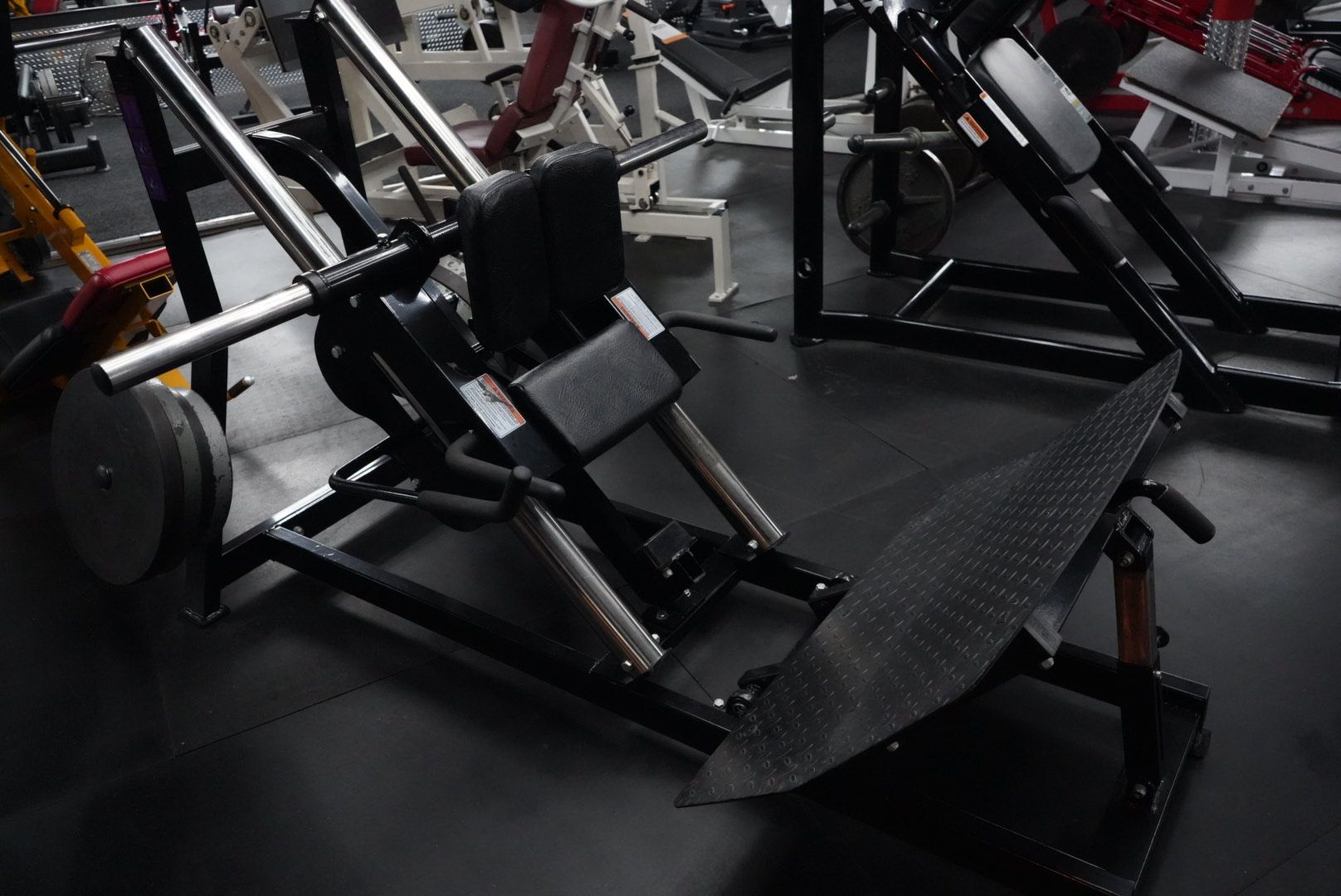 Black gym leg press machine with padded seat and footplate in a fitness center