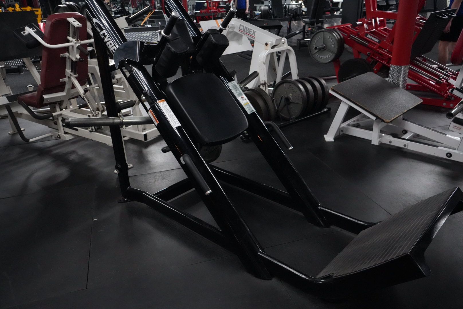 Black leg press machine in a gym with red and white weight equipment nearby