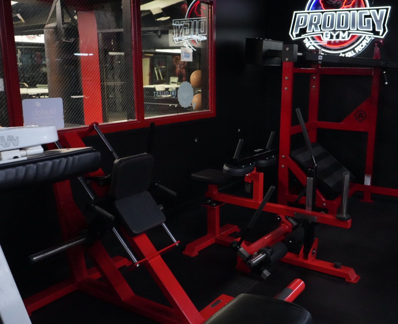 Red and black gym equipment in a workout room with a mirrored wall and Prodigy logo sign.