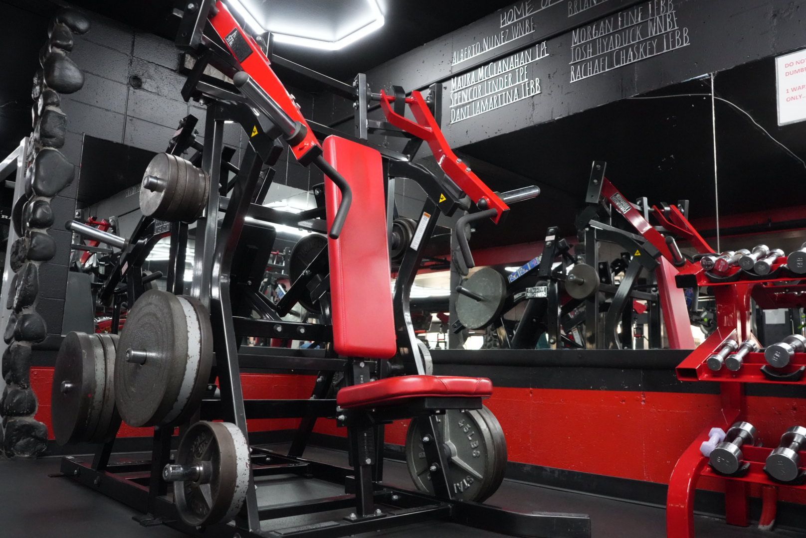 Red and black gym equipment arranged in a mirrored fitness room with weight machines and benches