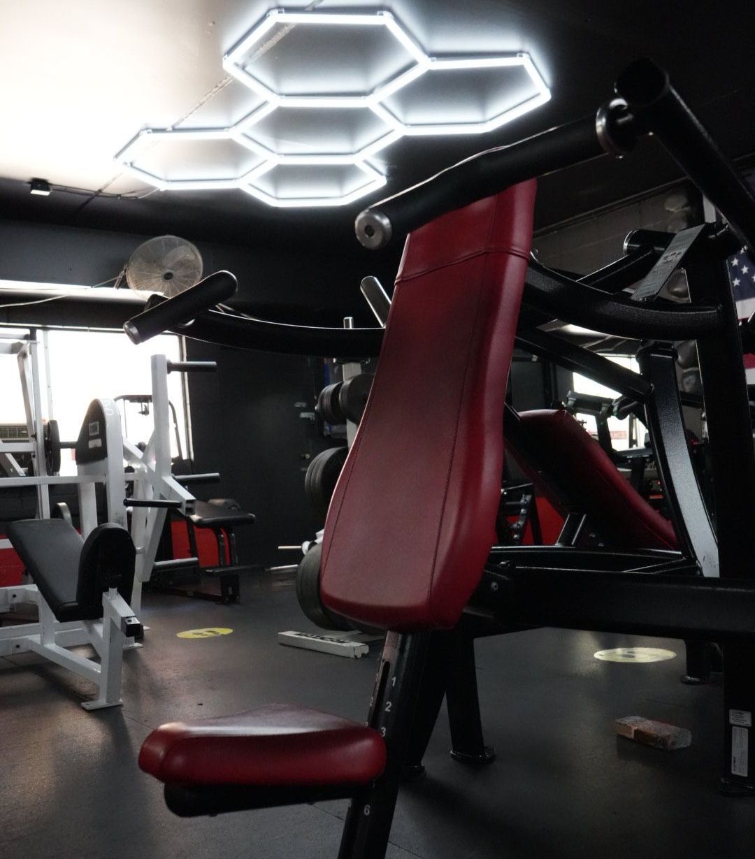 Gym interior with red workout machines and bright hexagonal ceiling lights