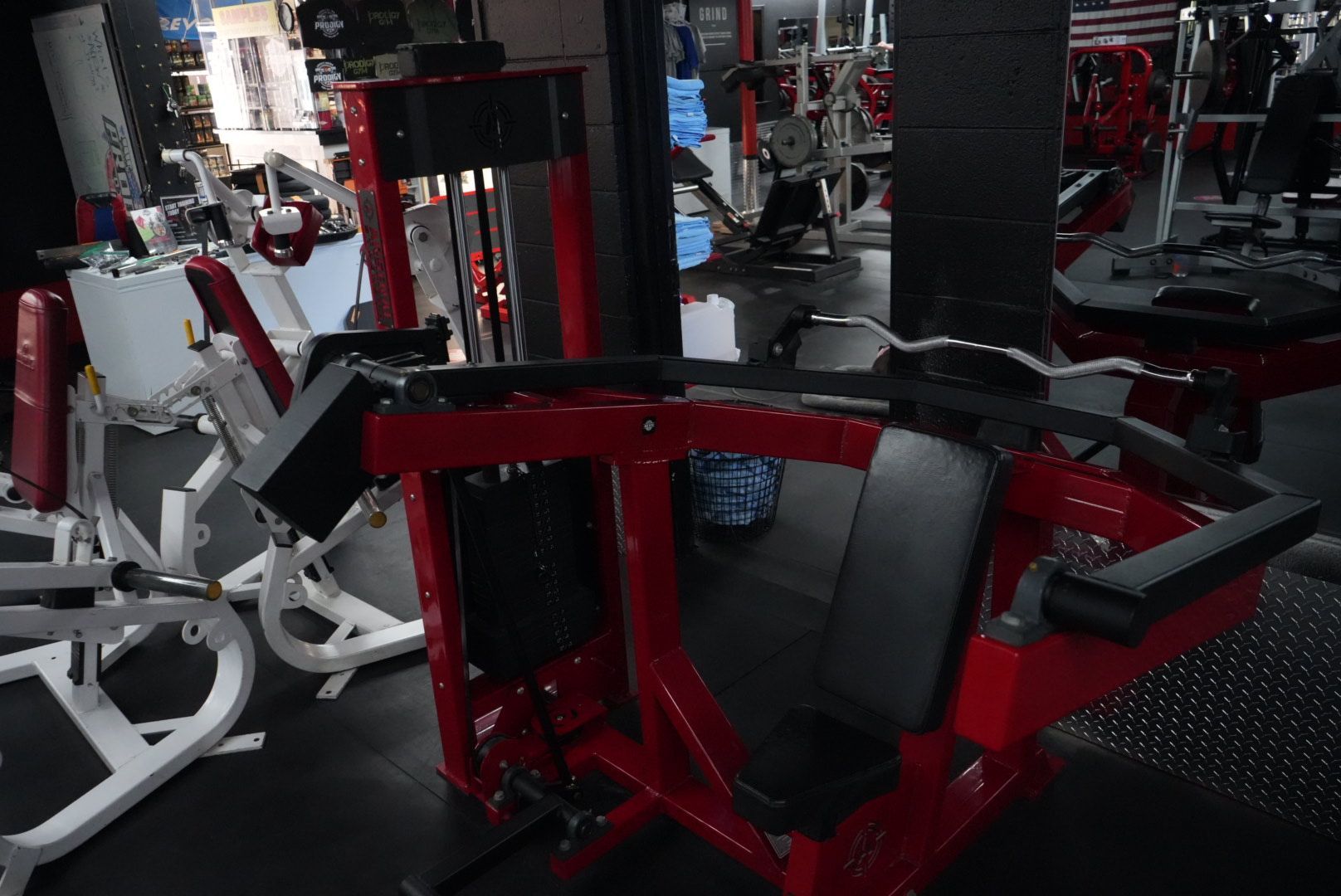 Red and black gym machine in a fitness center, surrounded by other exercise equipment.