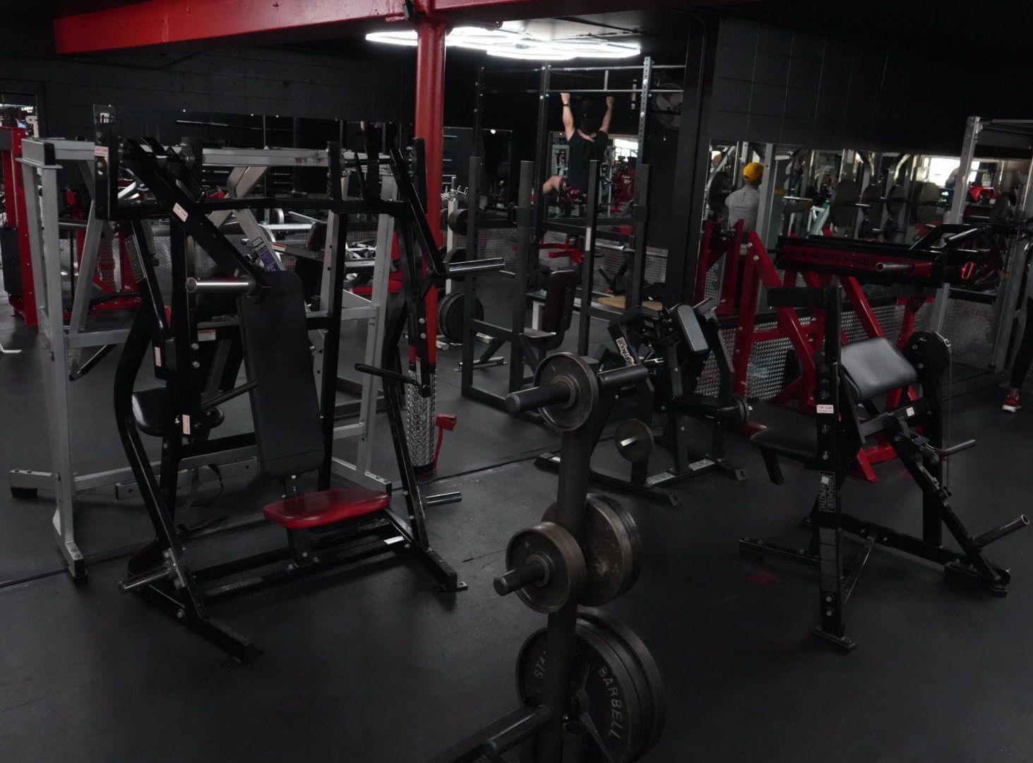 Dim gym interior with red-and-black workout machines and weights on dark flooring