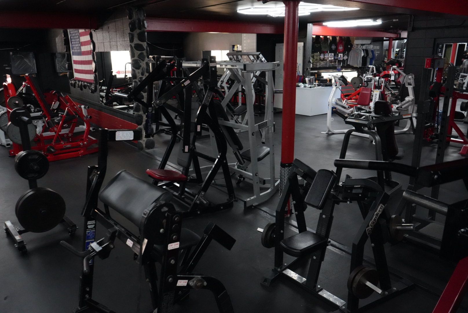 Dim gym with rows of exercise machines, black and red equipment, and mirrors along the walls.