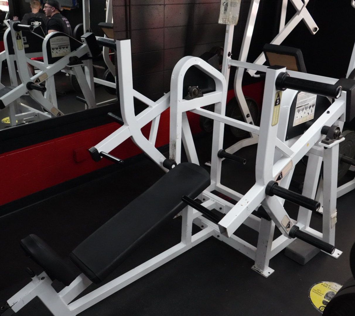 White gym leg press machine beside a mirror in a workout room