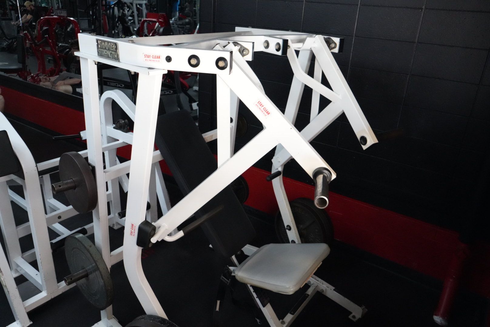 White gym exercise machine with padded seat and levers in a dark workout room
