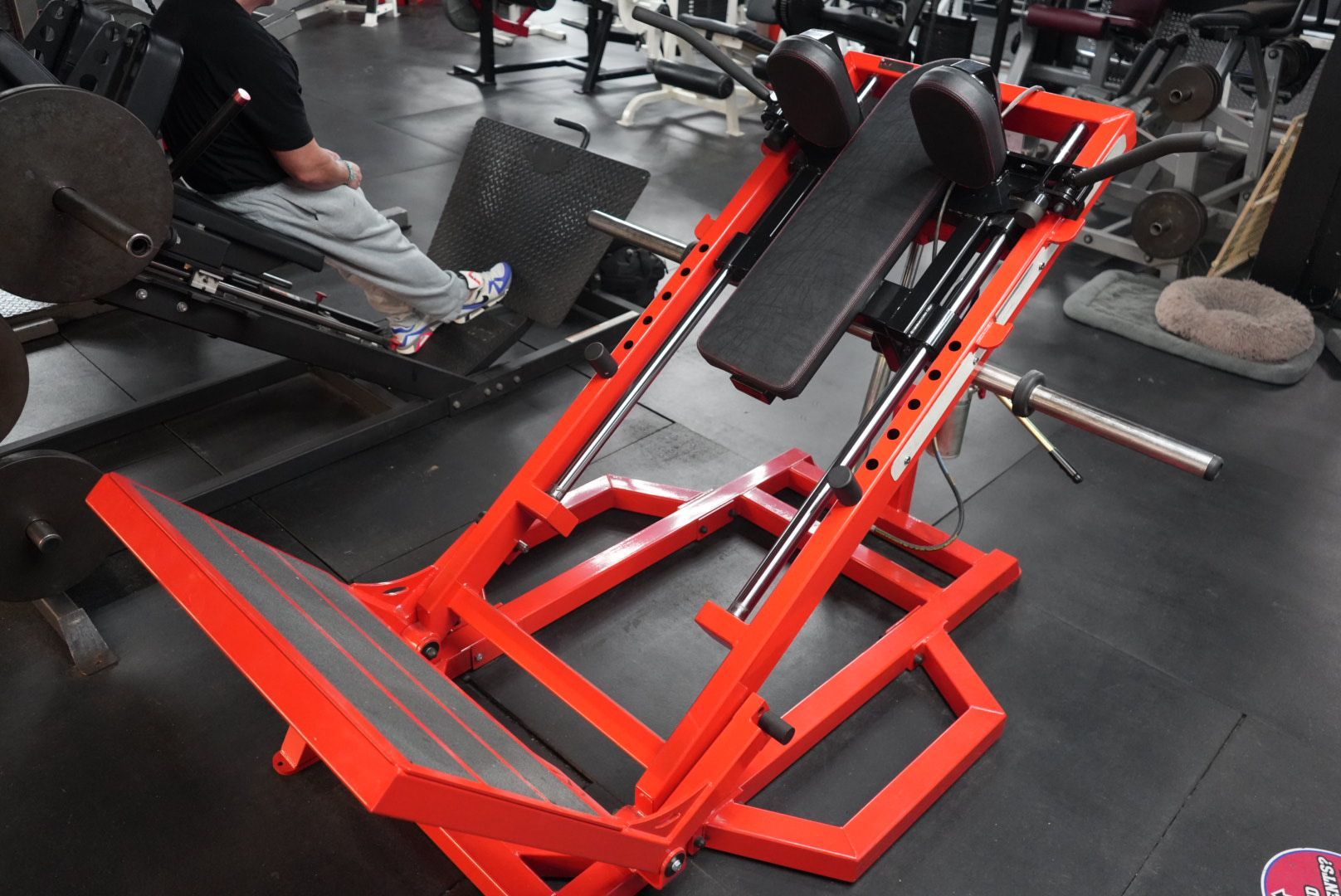 Red exercise leg press machine in a gym with a person seated on it