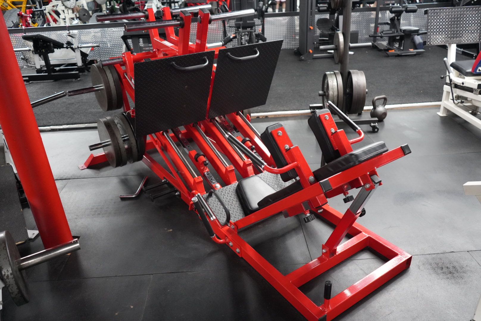 Red leg press machine in a gym, with black padding and weight plates loaded on the sides.