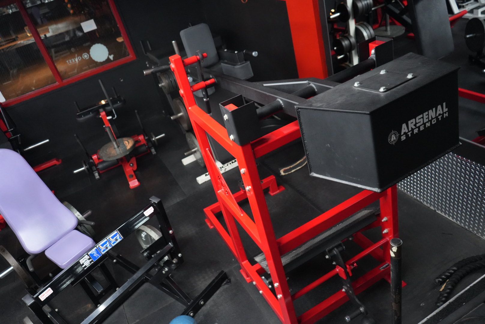 Red weight bench in a gym with black equipment and a dumbbell rack on the wall