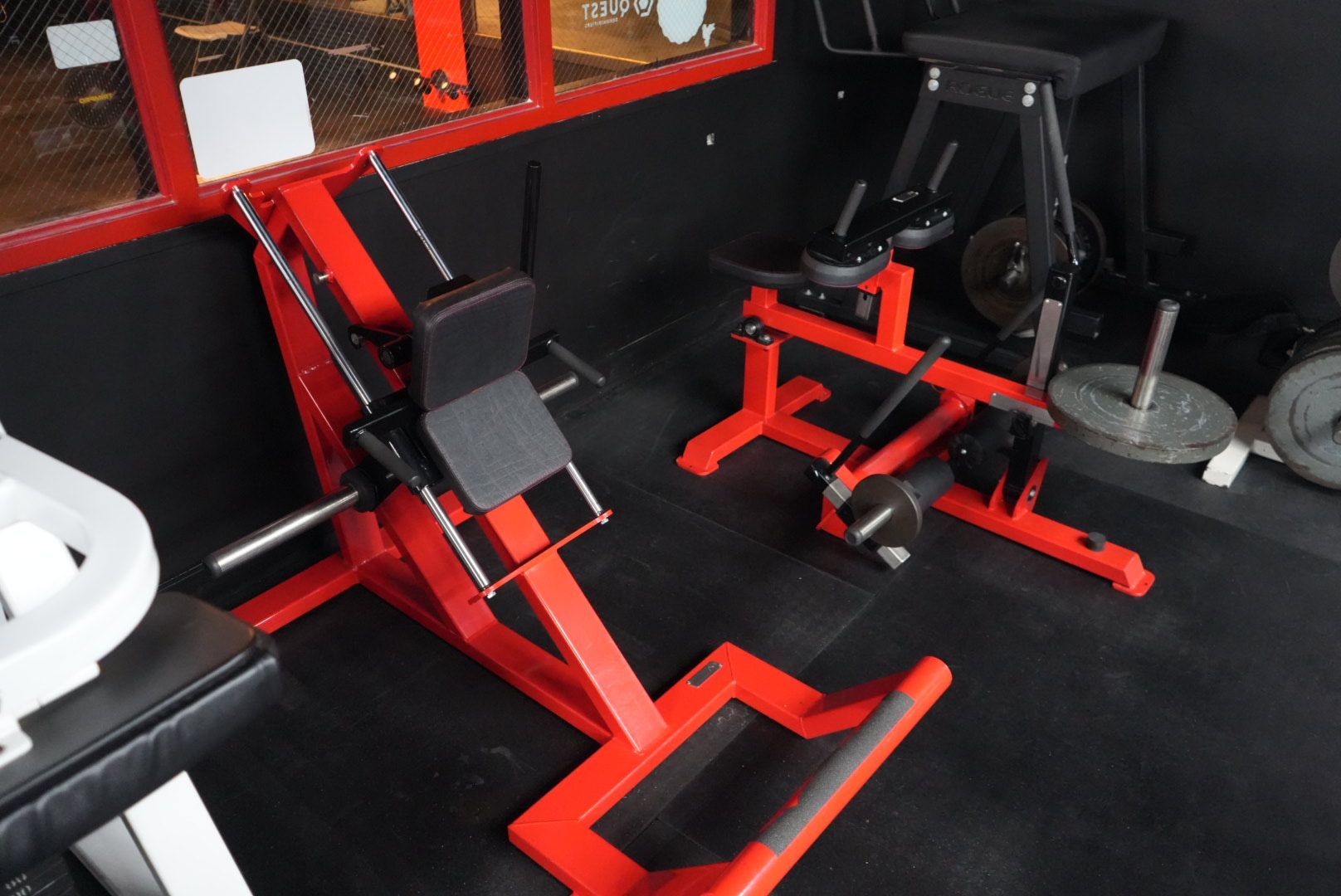 Red and black gym exercise machines in a fitness room with black flooring