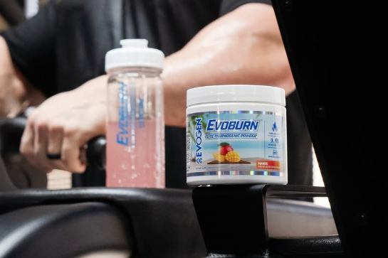 Gym supplement container and shaker bottle on a car console, with a person’s arm in the background