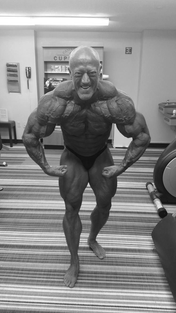 A black and white photo of a bodybuilder flexing his muscles in a gym.
